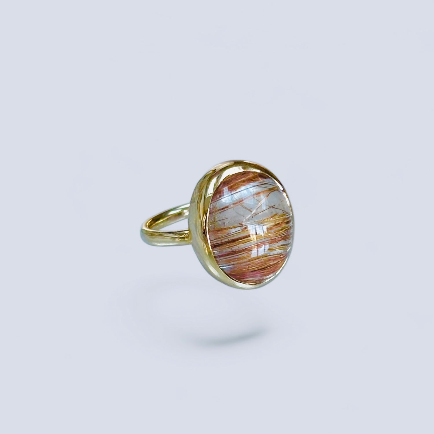 Gold ring with a golden rutilated quartz stone on a light gray background