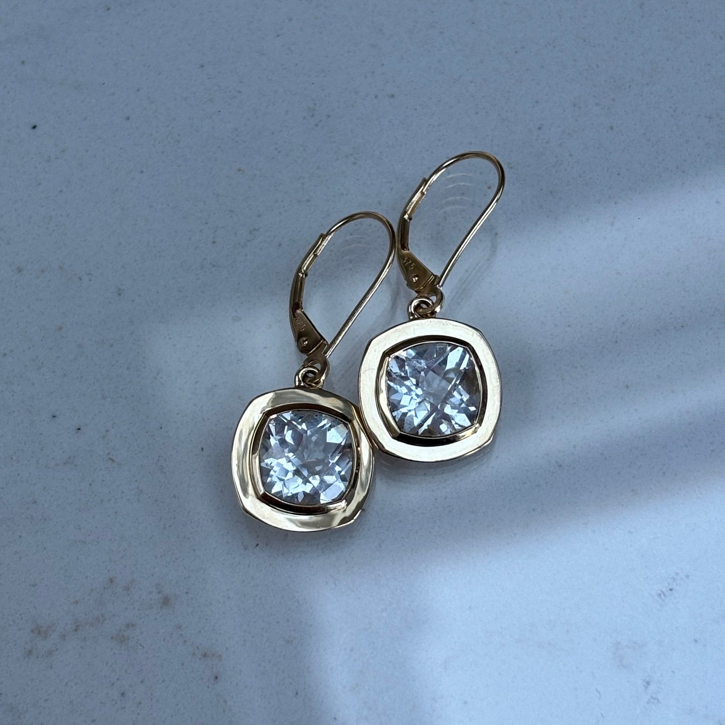 Gold earrings with clear topaz gemstones on a light gray background
