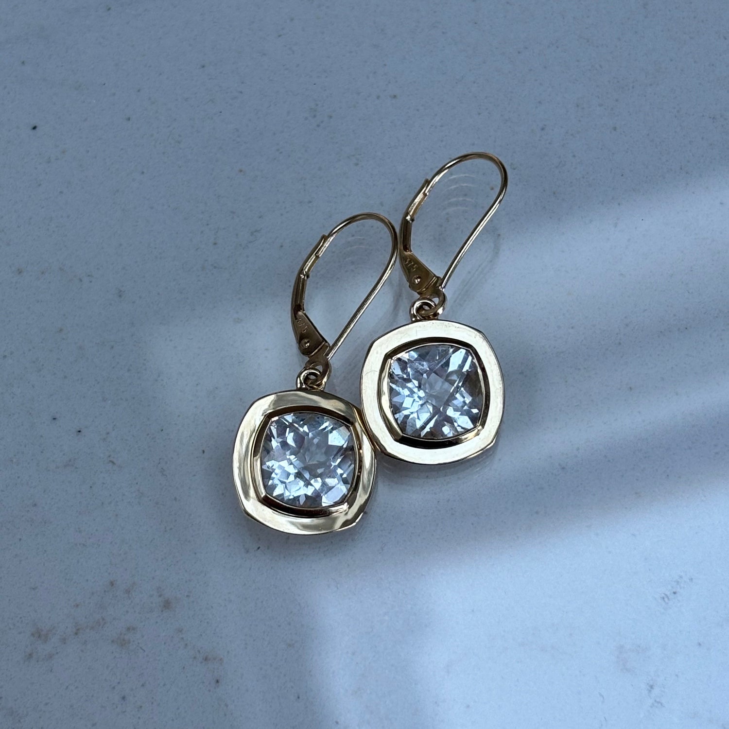 Gold earrings with clear topaz gemstones on a light gray background