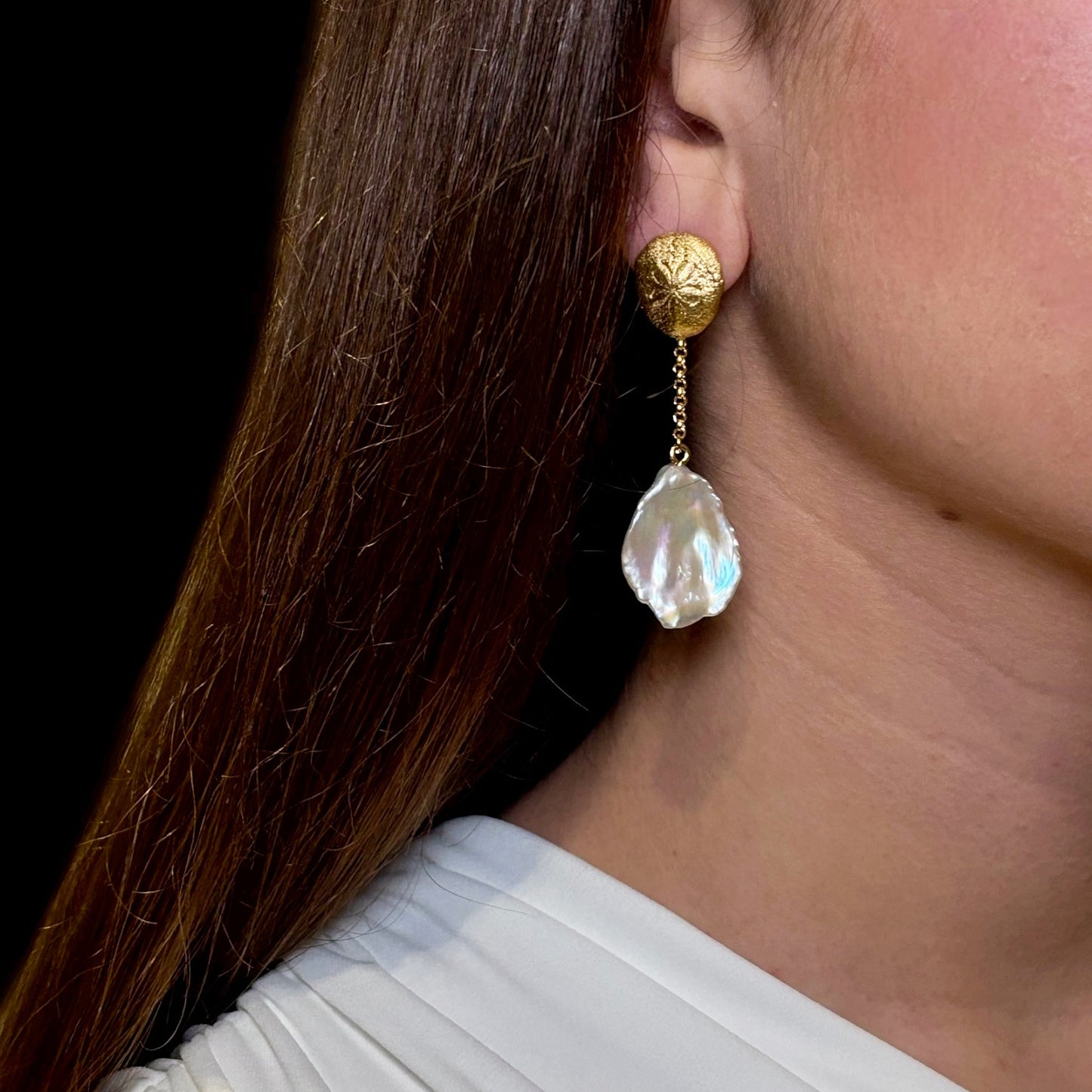 Gold earring with a pearl drop worn by a person against a neutral background