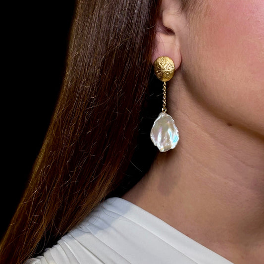 Gold earring with a pearl drop worn by a person against a neutral background