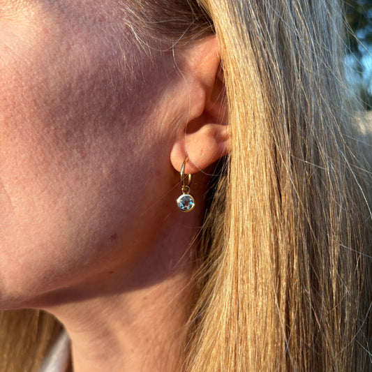 Close-up of an ear with an aquamarine earring, hair partially covering the face.