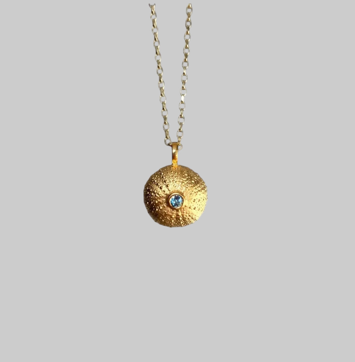 Gold necklace with a textured sea urchin pendant on a light gray background