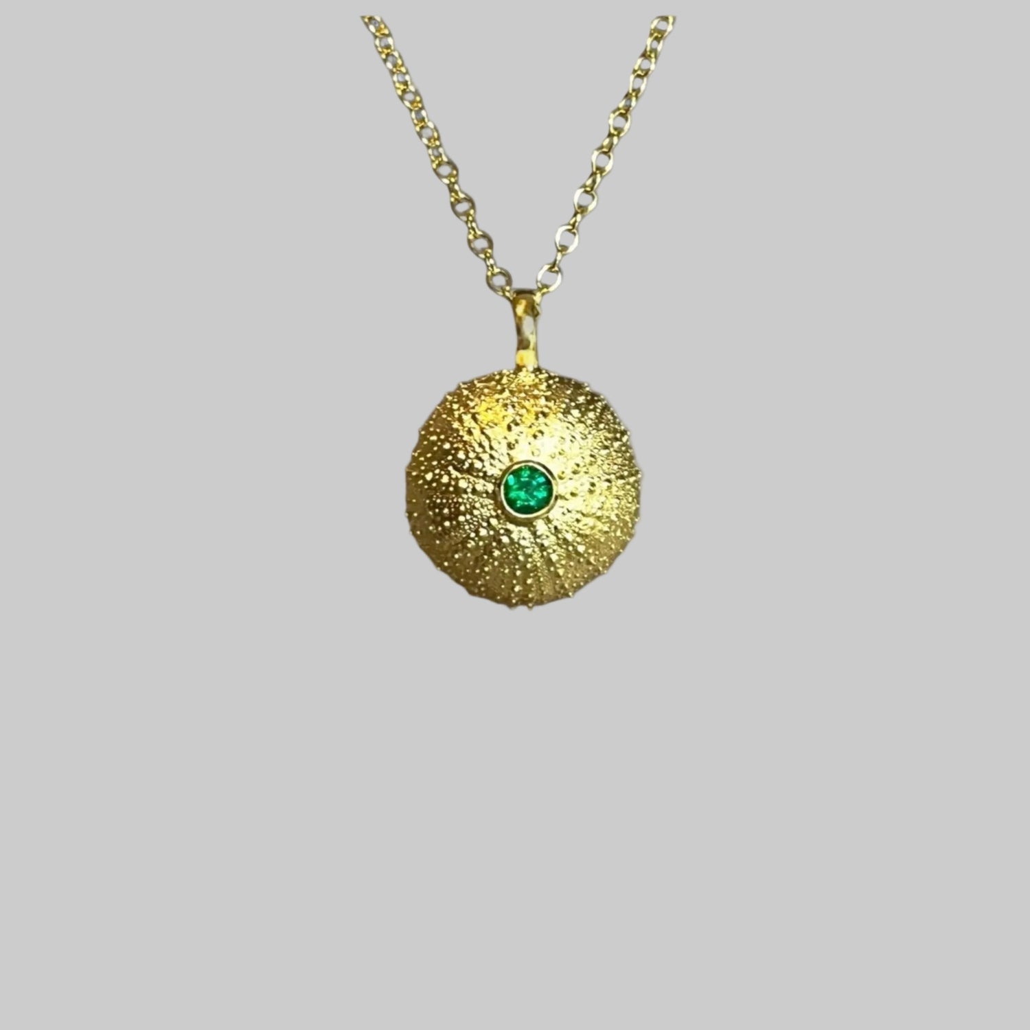 Gold sea urchin pendant necklace with a emerald on a light gray background