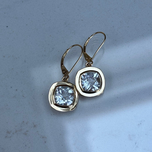 Gold earrings with clear topaz gemstones on a light gray background